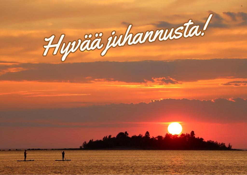 Kaksi ihmistä suppailemassa auringonlaskussa. Kuvan yläosassa teksti, jossa lukee hyvää juhannusta!