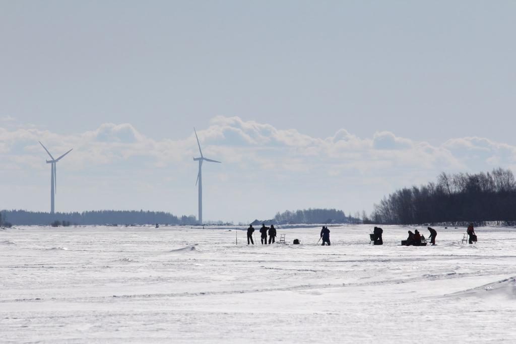 Talvinen kuva merenjäältä, tuulimyllyjä ja pilkkijöitä