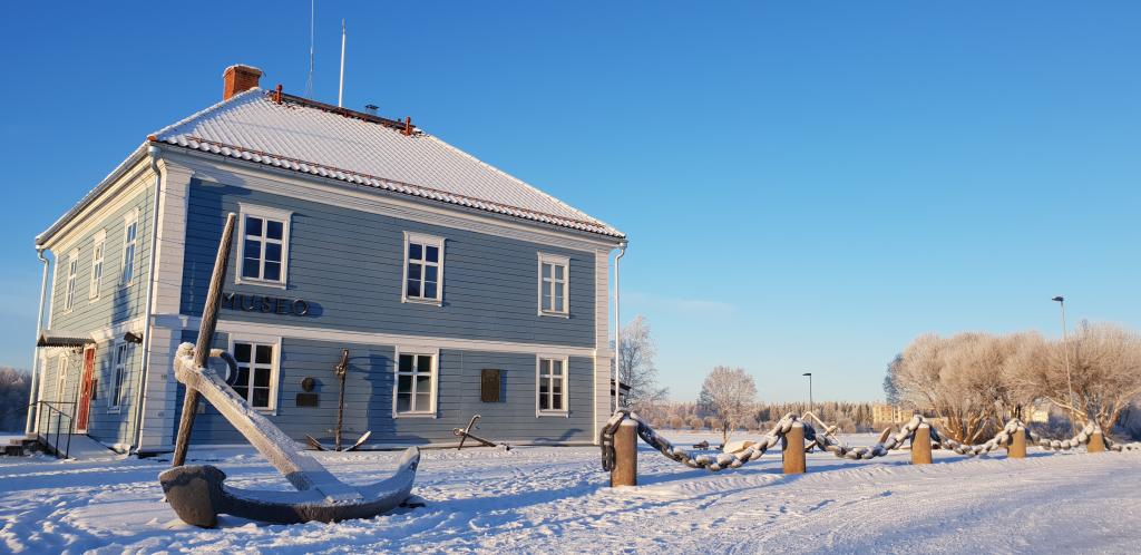 Museon sininen, kaksikerroksinen rakennus talvimaisemassa.