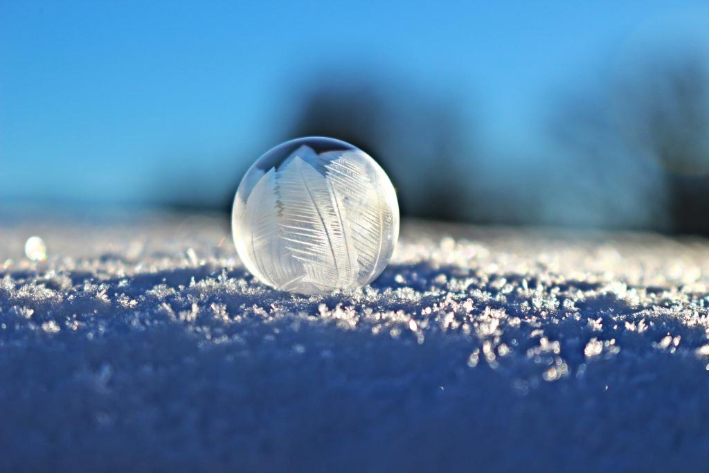 Lähikuva saippuakuplasta lumessa, taustalla sininen taivas.