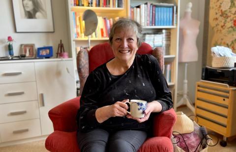 A smiling woman sitting home with a cup of coffee in her hand.