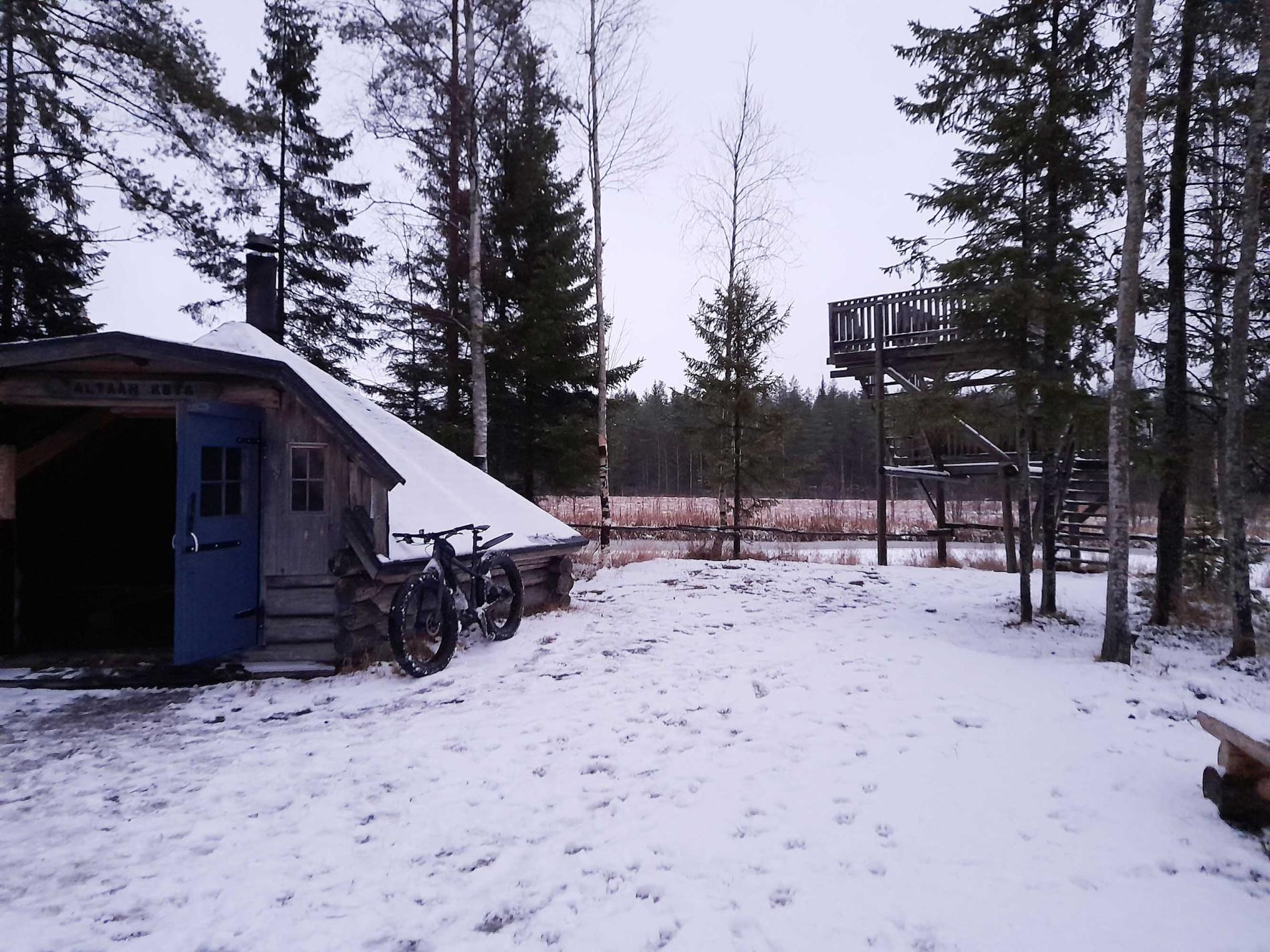 Fatbike nojaamaassa kotarakennusta vasten hämärtyvässä illassa.