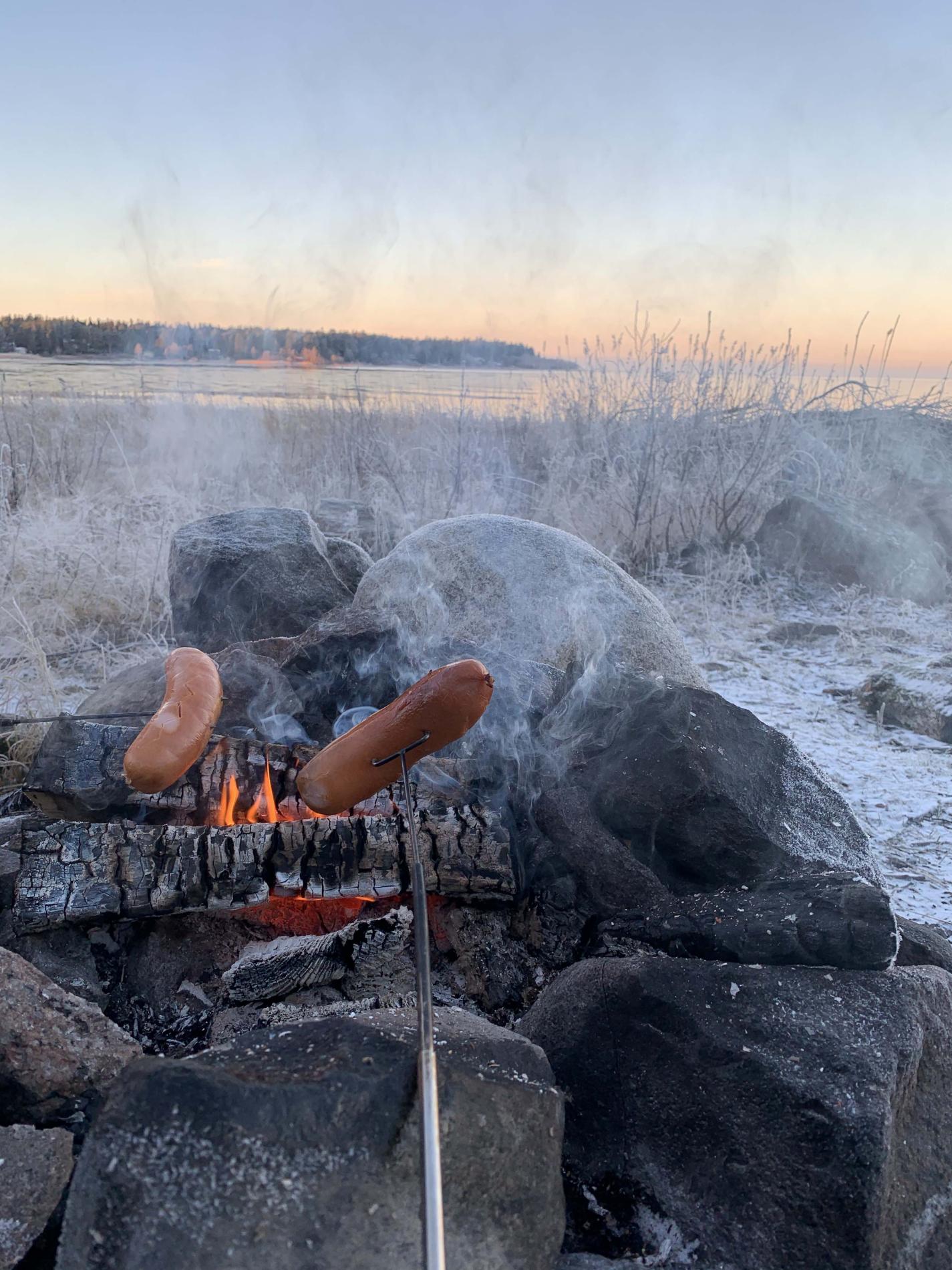 Makkaraa paistamassa hiilloksella meren rannalla.